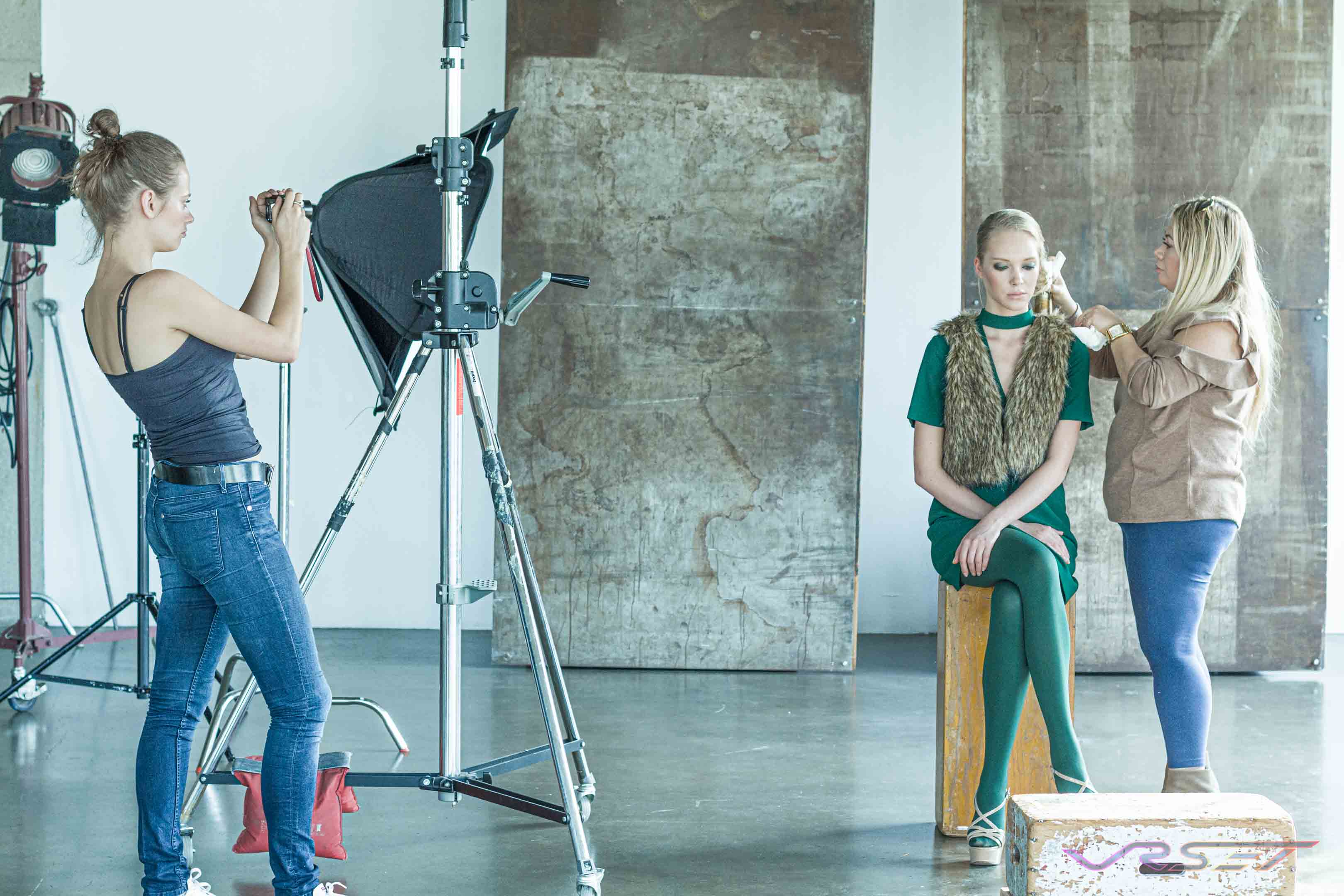 Professional Makeup Artist Working On The Models Face While An Assistant Holds A Wirless Strobe At A Los Angeles Clothing Photography Studio Makeup touch up while an assistant positions a softbox on a stand